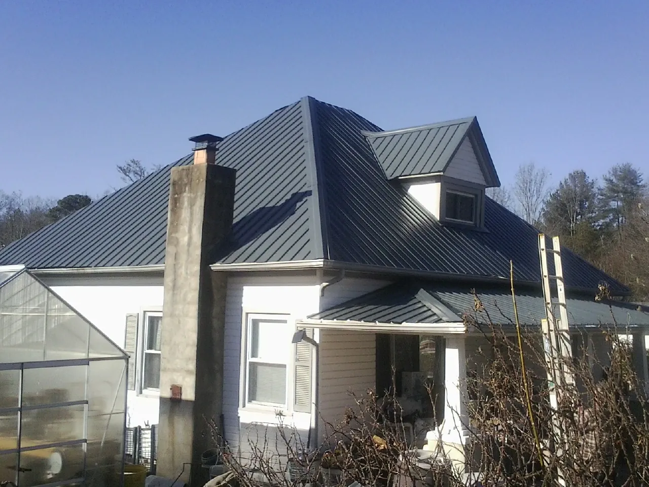 Dark blue standing seam metal roof on a white farmhouse with dormer — Slate & Tile Roof Repair by Roofing Brothers in Ridgeland