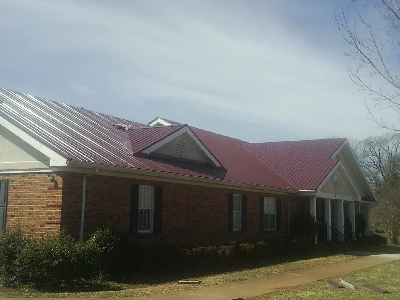 Red metal roof with gabled entries on a long brick building, from a Hail Damage Roof Repair job in Ridgeland