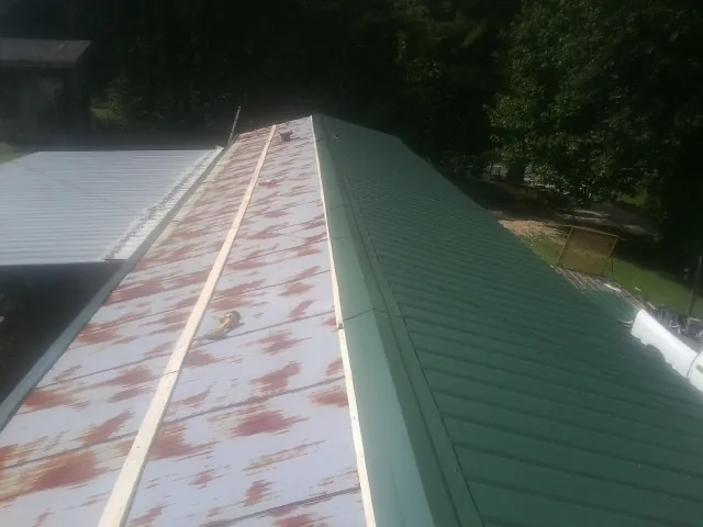 Old rusted panels beside newly installed green metal roofing — Wind Damage Roof Repair by Roofing Brothers in Ridgeland