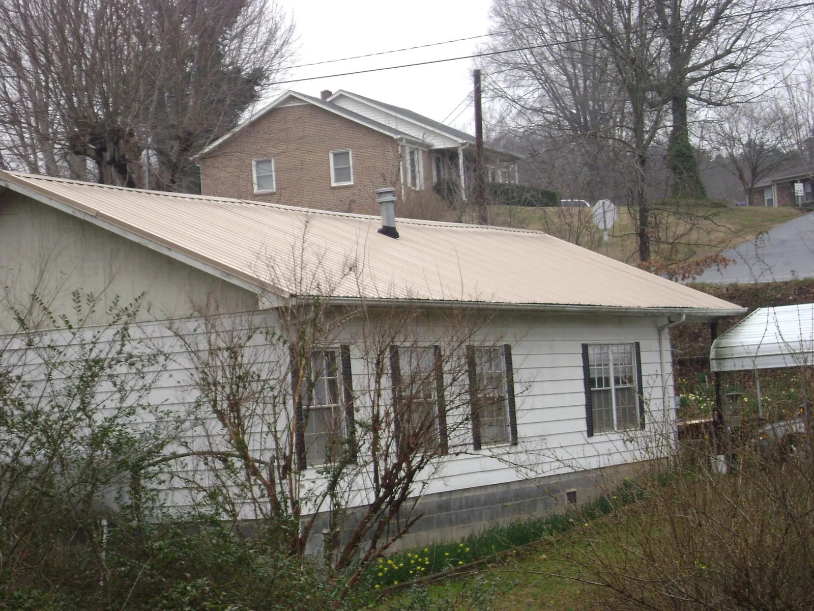Tan metal roof on a white sided house set into a hillside — Commercial Roofing by Roofing Brothers in Ridgeland